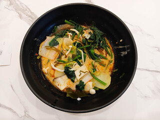 Spicy mala soup served in a black bowl, filled with vegetables and herbs, rich chili broth, hot flavor, Asian comfort food style.