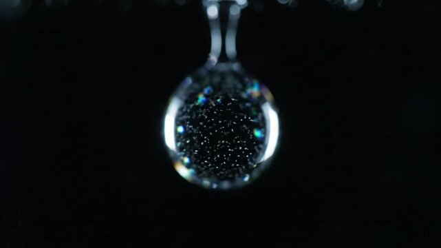 Close-up of a single water droplet with microbubbles creating a shimmering effect against a dark background.