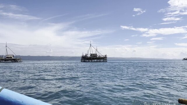 a long-range shot from a moving boat captures a traditional Indonesian fishing platform, locally known as a bagang, floating in the middle of the sea. 