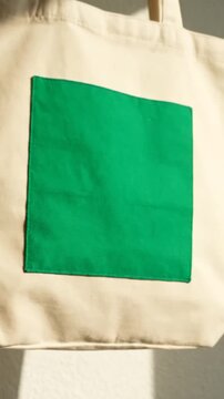 Beige canvas tote bag with green patch on textured wall