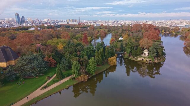 Aerial drone forward of &Icirc;le de Reuilly and the Temple of Love in Bois de Vincennes. The colorful autumn park and lake contrast with the Paris skyline in background, France
