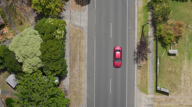 Drone footage showcases Boronia Street in Melbourne from above, highlighting a vibrant red car on a clear road surrounded by lush greenery. Perfect for urban and travel themes.