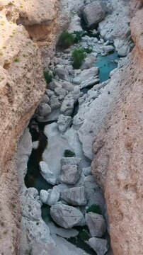 Vertical aerial of beautiful Wadi Bani Khalid oasis with turquoise water, hidden river between mountains and palm trees in the Sultanate of Oman.