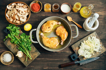 Fried seasoned chicken legs in a pan on a wooden table with chopped ingredient