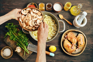 Hands adding sliced mushrooms to a pot with onions while cooking in a kitchen