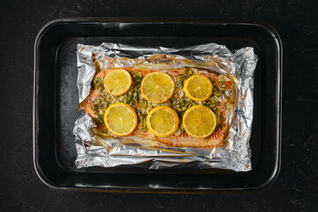 Cooking pink salmon with lemon slices on a baking sheet lined with foil in the kitchen