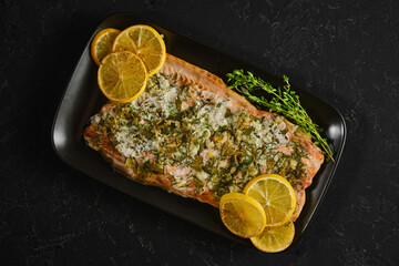 Pink salmon dish with herbs and lemon on a black plate for a tasty meal idea