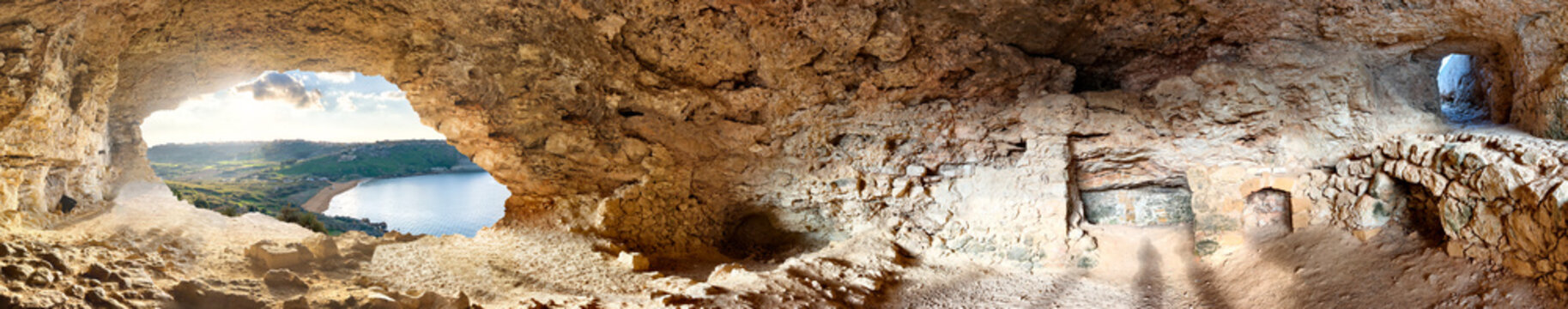 Panoramic shot of Tal-Mixta Cave with view of Ramla Bay, green hills and blue sea in sunlight