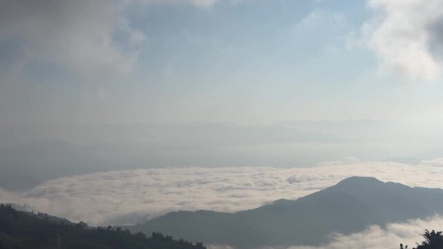 A breathtaking 4K horizontal timelapse capturing a majestic mountain range sandwiched between two layers of clouds. The lower sea of clouds flows rapidly like a white river through the valleys, while 