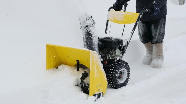 Slow motion video of unrecognizable man in felt boots removing snow from path with snowplow machine. Winter home maintenance and snow removal job in a suburban neighborhood