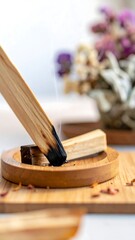 Burning wood incense stick releasing smoke, with dry flowers in the background