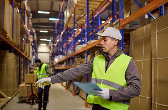 Warehouse logistics worker checks inventory and storage. He directs loading on shelves, guiding boxes and shipping for accurate delivery. Lean logistics ensure safe organized workflow.