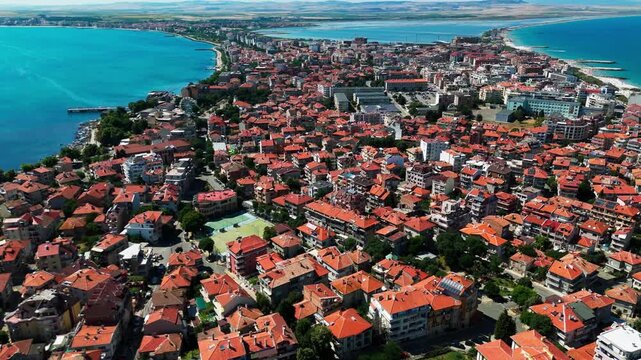 Vast aerial view of Pomorie with terracotta rooftops, sea on multiple sides, and the distant mainland visible on the horizon.