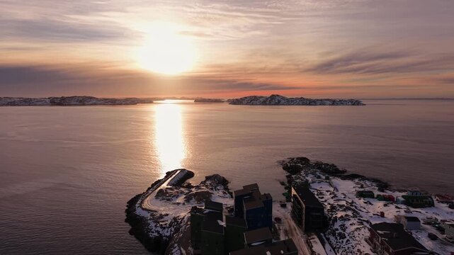 Traditional and modern colorful houses nestled on the rocky shores of Nuuk. The golden hour light illuminates the snowy landscape and the calm fjord waters.