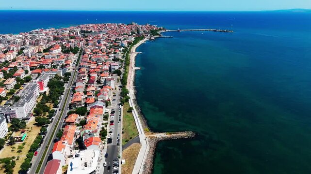Drone follows the Pomorie coastline, showcasing terracotta-roofed buildings beside the vast Black Sea under clear skies.