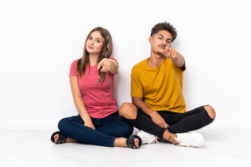 Fototapeta premium Young couple sitting on the floor isolated on white background pointing front with happy expression