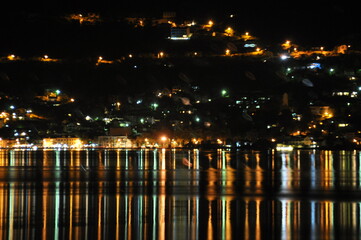 Night scene of a vibrant lakeside town with reflections illuminating the water surface