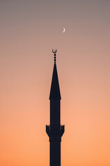 Minaret silhouette with crescent moon against sunset sky