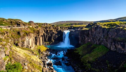 Obraz premium A stunning view of a powerful waterfall cascading into a deep canyon under a clear blue sky. Rugged cliffs frame the scene