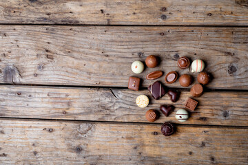 Top view of varied chocolate spheres in a heart shape on wood with space for text
