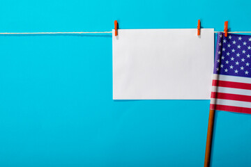 Fototapeta premium Blank paper with copy space hanging by america flag hanging from clothesline on blue background