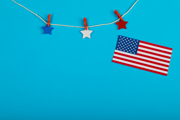 Clothespins holding star shapes on string by america flag with copy space on blue background