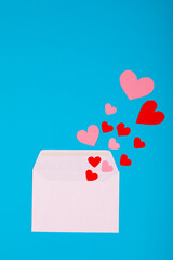Overhead view of pink and red hearts coming from white envelope on blue background with copy space