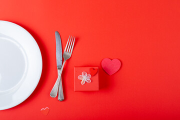 Overhead view of place setting by gift and heart shaped decoration on red background, copy space © wavebreak3
