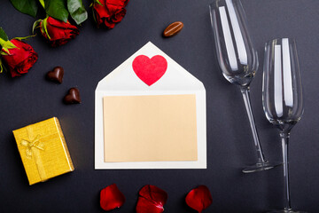 Overhead view of blank letter and champagne flutes by red roses on table, copy space