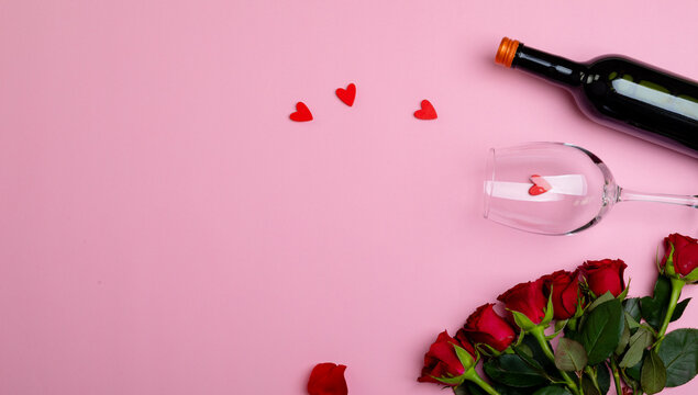 Overhead view of wine bottle and glass with red roses isolated on pink background, copy space