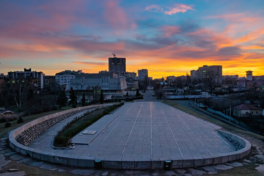 Cherkasy urban view at twilight, showing city architecture and a large paved public square, with vibrant orange and blue clouds painting the sky during a colorful sunset