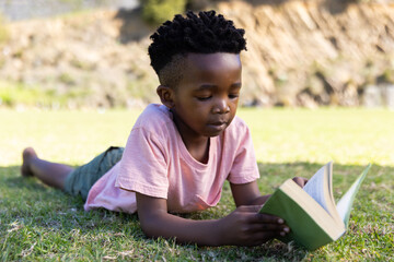 Outdoors, Reading book, african american boy lying on grass outside, enjoying leisure time