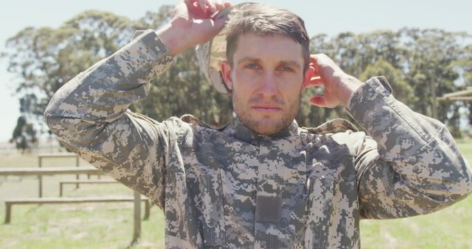 Portrait of caucasian male soldier in combat uniform and cap standing on army obstacle course