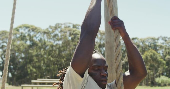 Fit african american male soldier with deadlocks climbing down rope on army obstacle course