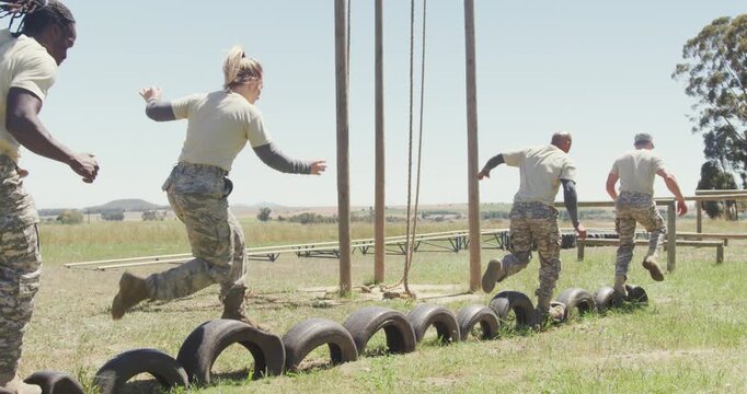 Diverse group ale soldiers running on car tyres at army obstacle course in the sun