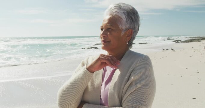 Thoughtful senior hispanic woman standing on beach and look into distance