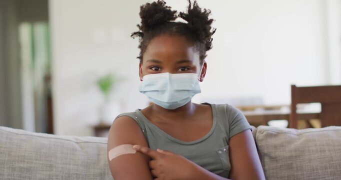 African american girl wearing face mask pointing at bandage on her arm