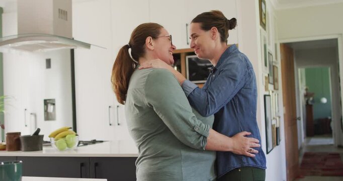 Caucasian lesbian couple smiling and dancing in kitchen