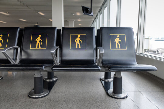Row of airport seats marked with yellow elderly icons in a bright terminal waiting area. Priority seating reserved for seniors and passengers needing assistance. Travel and accessibility theme