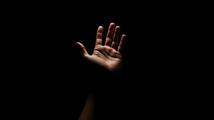 Fototapeta premium A raised hand illuminated by intense orange light against a deep black background, symbolizing a powerful stop gesture against violence and gender-based abuse. Used for the International Day for the