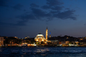 Fototapeta premium Sultanahmet district in twilight. Illuminated Yeni Camii, or New mosque, view from the cruise boat at Bosphorus.