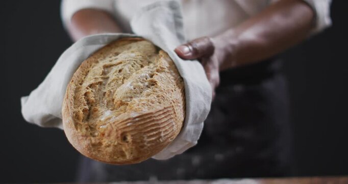 Video of cook holding loaf of bread on black background