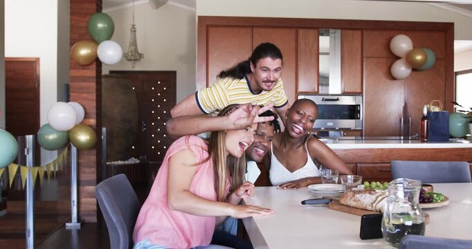 At party, Friends gathered in kitchen, smiling and looking at smartphone together