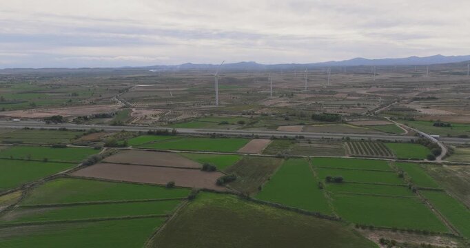Aerial view over agricultural plains in Spain with patchwork fields, roads and distant hills stretching toward the horizon in soft light