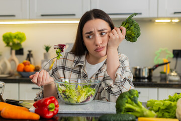 Young woman eats vegetable salad and looks drained after strict keto diet, craving comfort food....