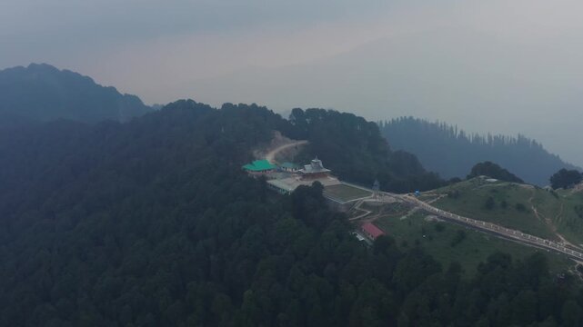 Overhead wide shot captures Hatu Mata Temple perched on forested peak, surrounded by dense pine-covered hills, winding paths, and hazy mountain ridges.