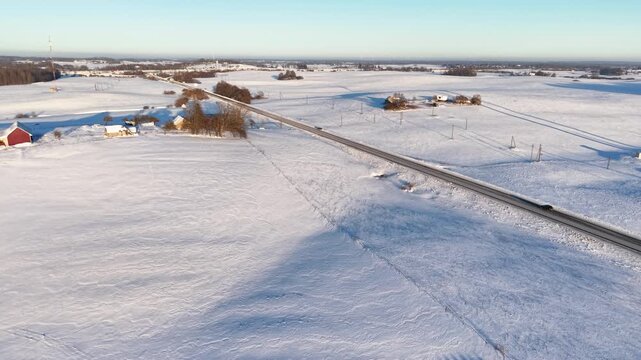 Drone video capturing a serene snowy landscape with a long road cutting through vast snowfields under a clear blue sky. The tranquil winter scene offers a peaceful and expansive view.