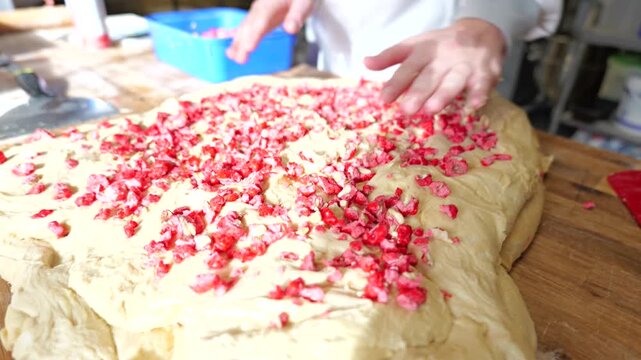 Close-up of baker hands spreading pink praline over raw dough