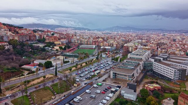 Aerial drone glide over El Baix Guinard&oacute; in Barcelona, Spain, showing dense residential buildings and the Camp Municipal de Futbol del Guinard&oacute; soccer pitch within the city fabric.