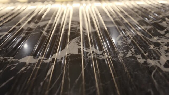 Close up of dark marble wall with white veining and vertical grooves lit by warm linear lighting, pan right shot